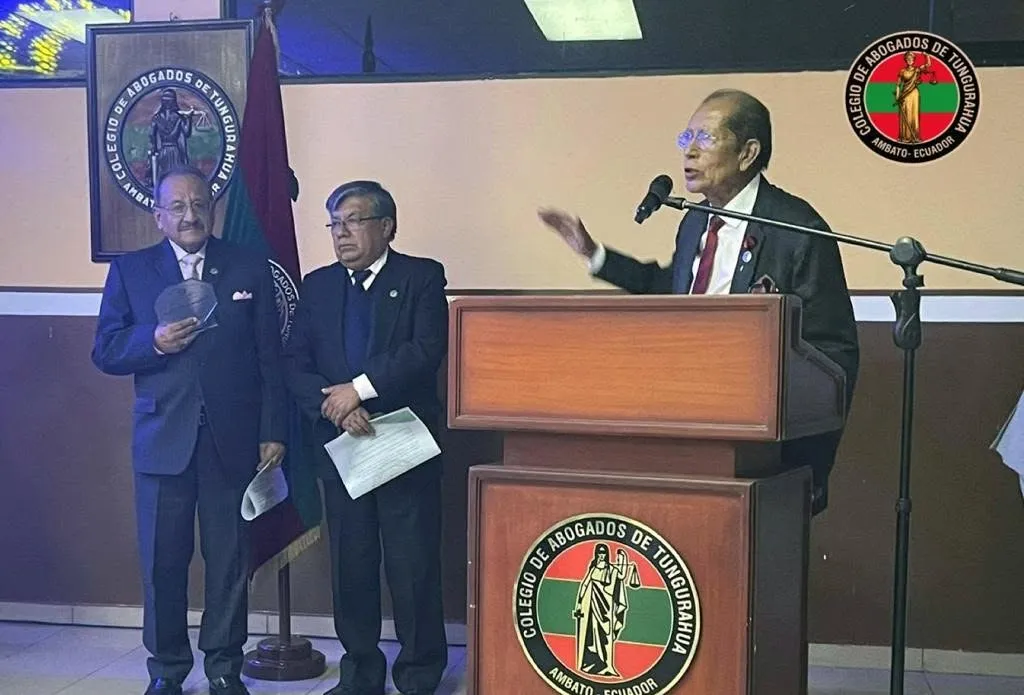 Orador en el podio con el emblema del Colegio de Abogados de Tungurahua, acompañado por dos abogados
