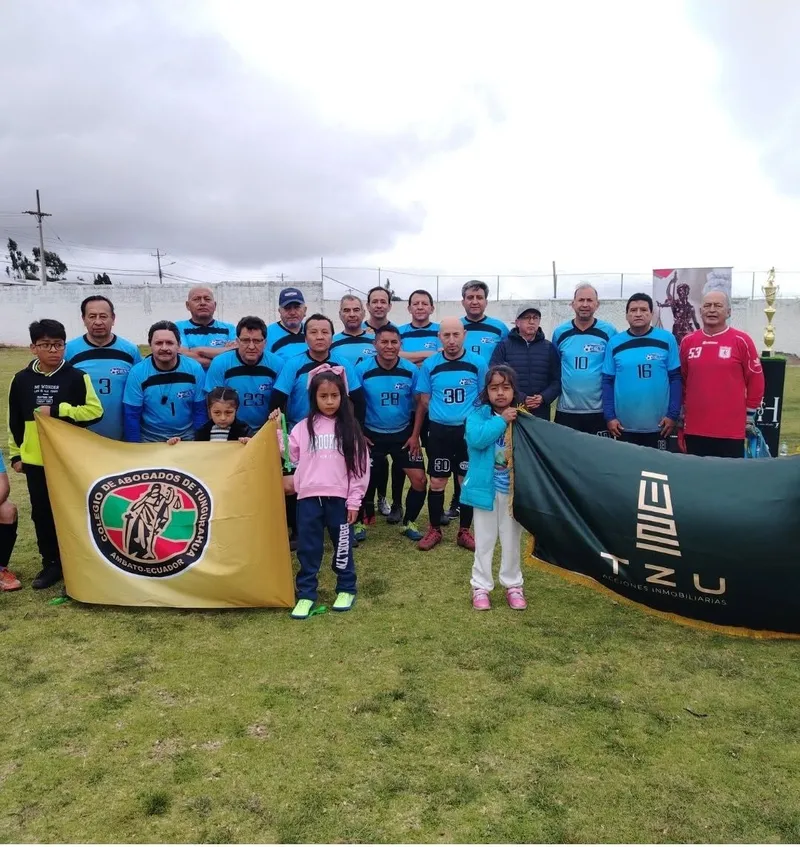 Equipo de fútbol con camisetas celestes posa con la bandera del Colegio de Abogados de Tungurahua y la del auspiciante en una cancha