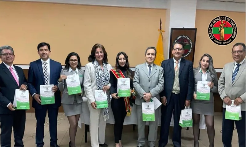 Grupo de abogados y abogadas posando con carpetas y certificados en el salón del Colegio, junto a la bandera de Ecuador